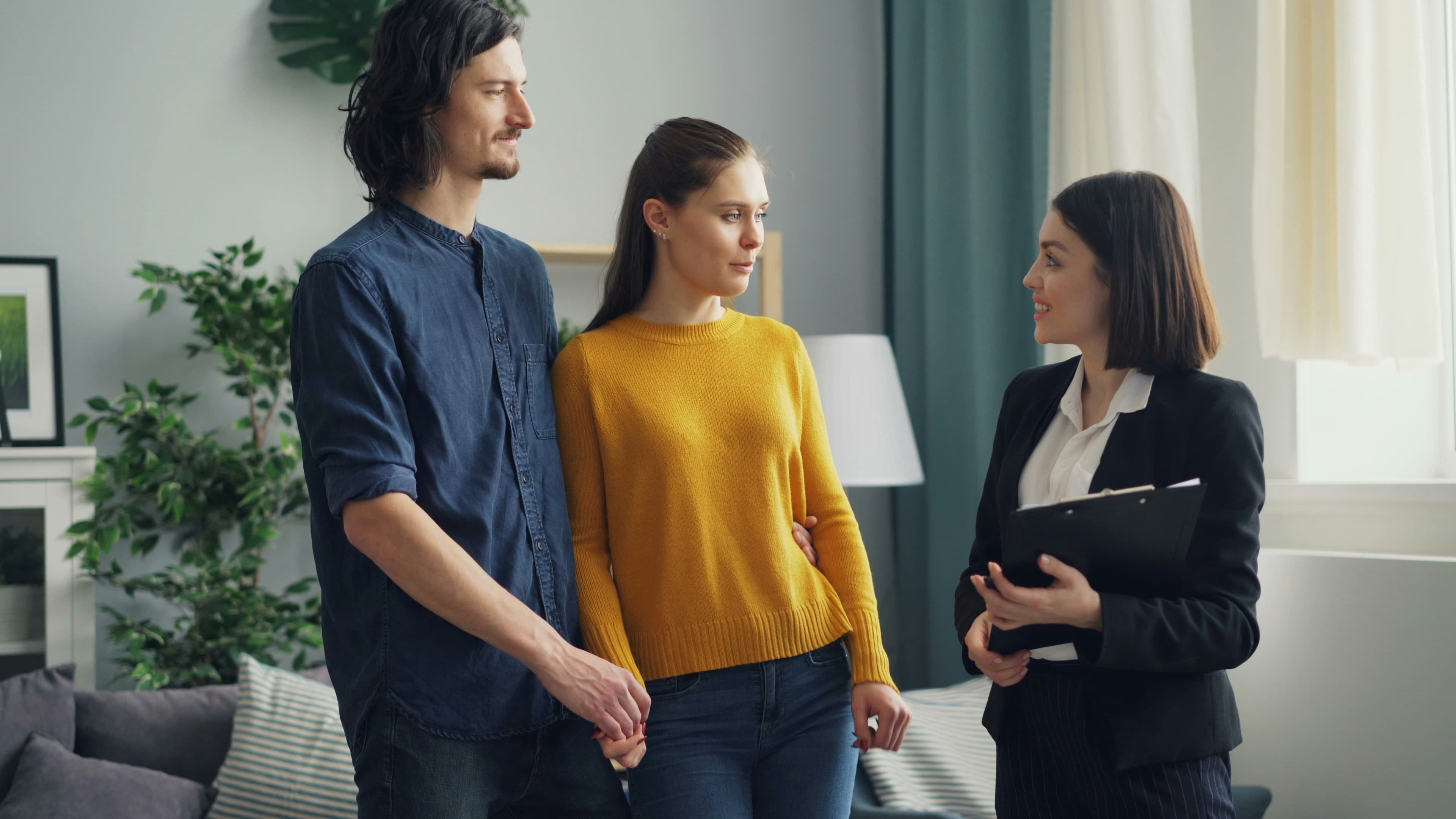 A couple meeting with their named personal manager, clipboard in hand, plants in soft light