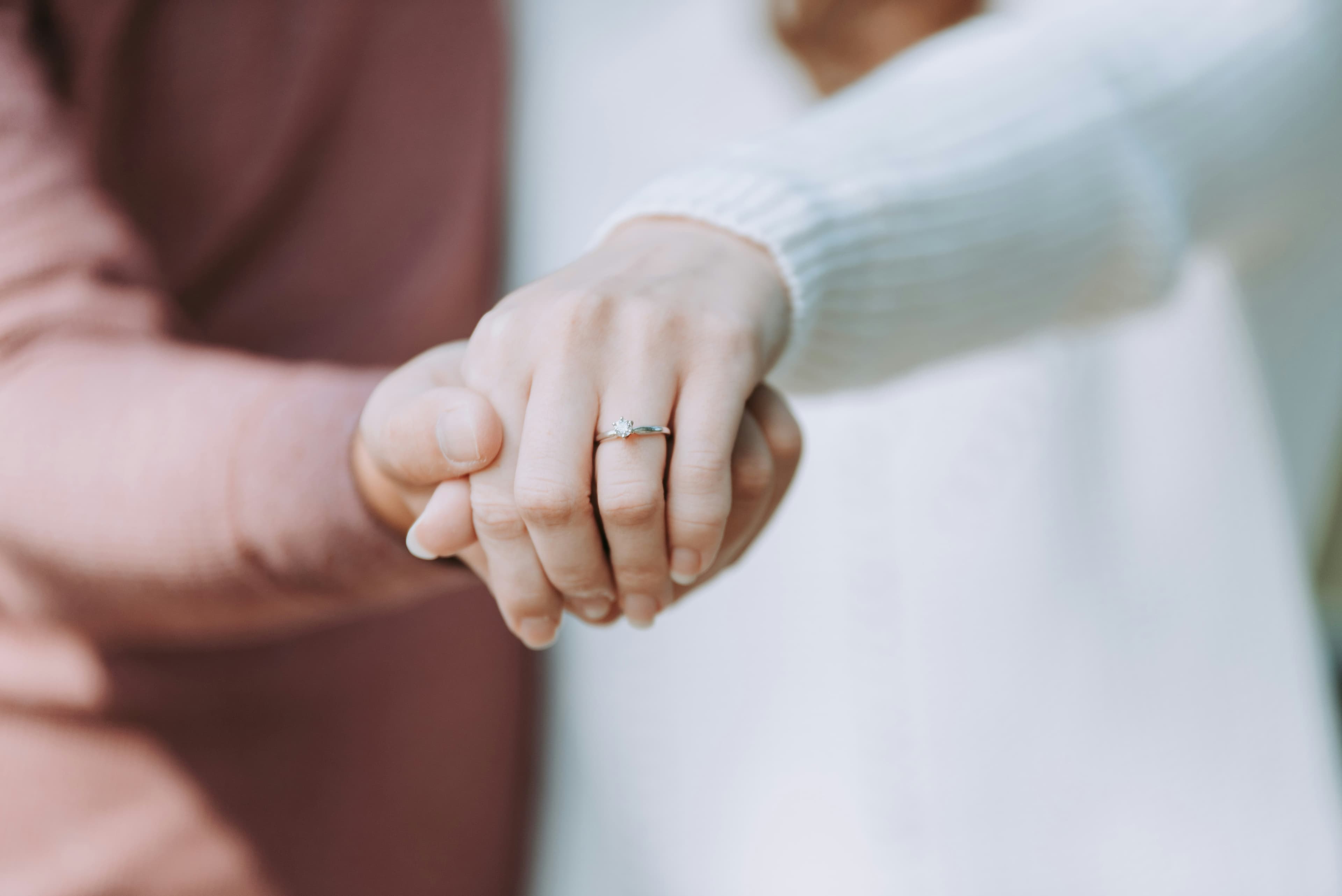 Two hands held quietly between them, an engagement-ring detail - commitment without ceremony