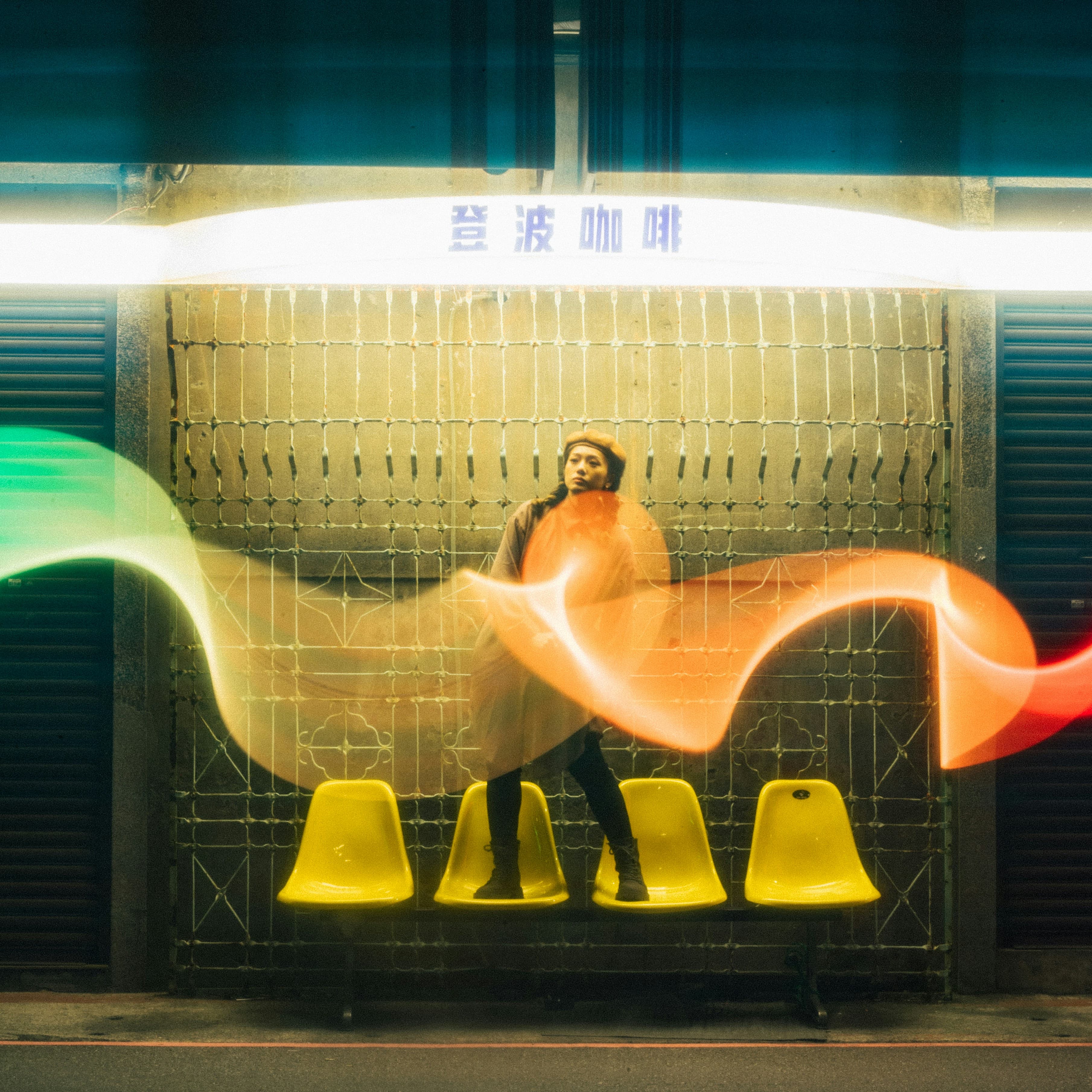 A figure at rest in an urban scene at night, light trails painting motion around them - a sense of ongoing presence